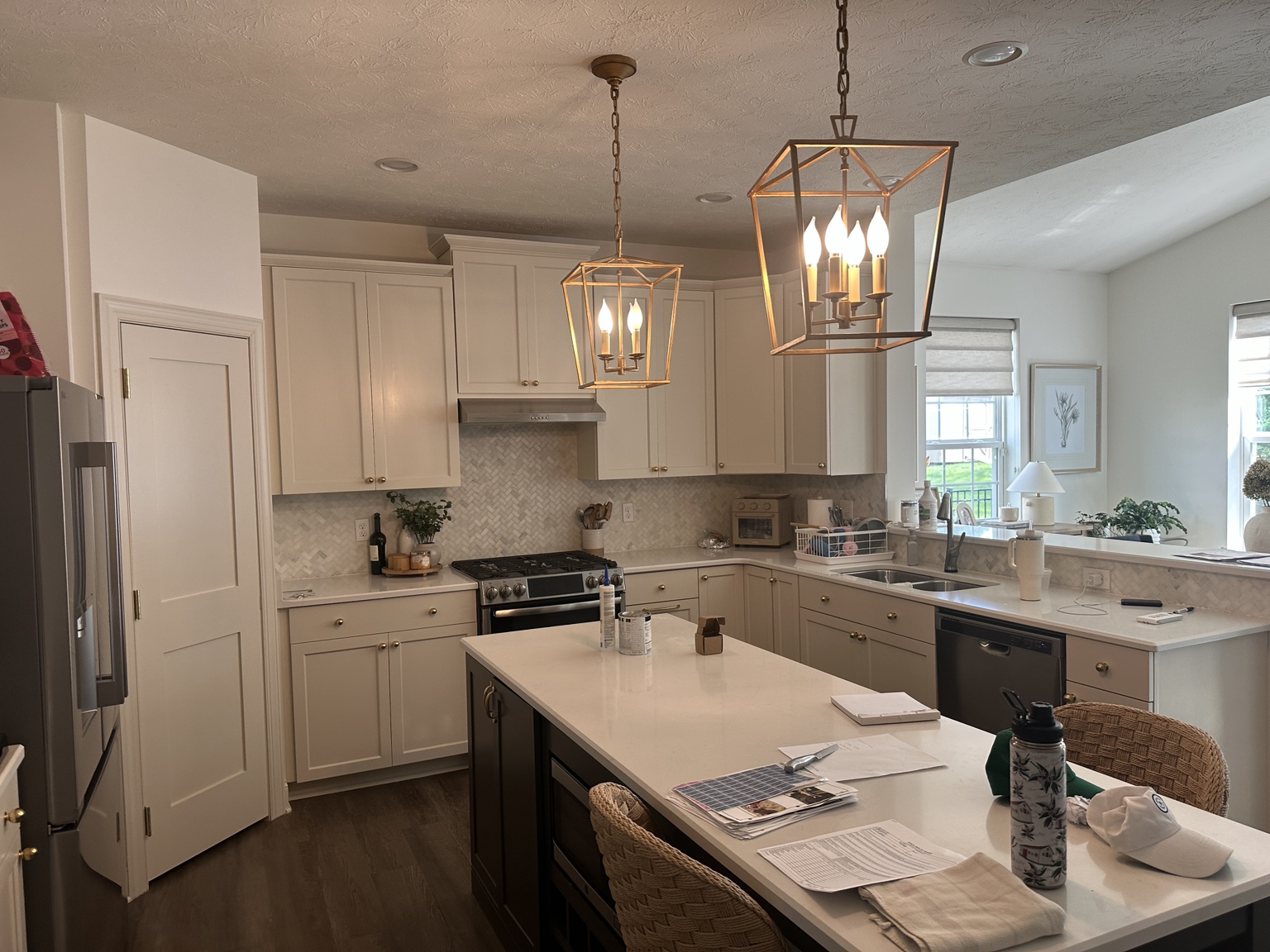 White kitchen cabinetry with gold hardware, pendant lights, and a contrasting dark island