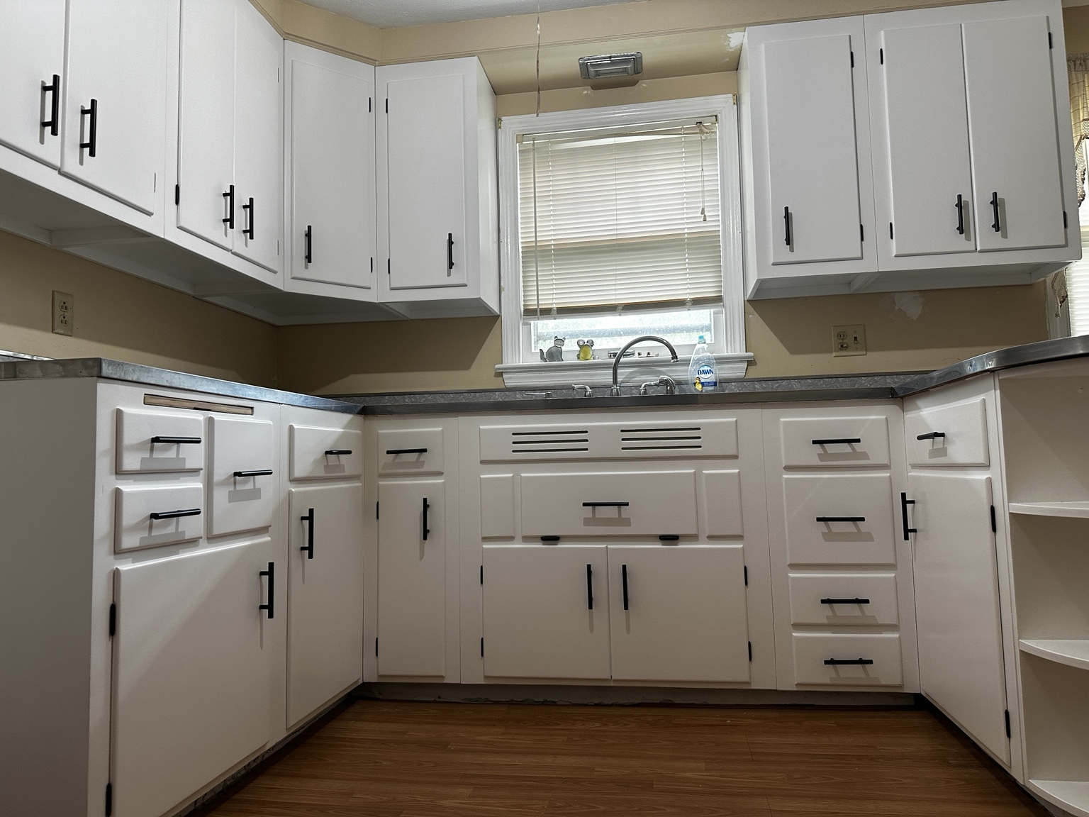 White kitchen cabinets around a sink with black pulls and exposed black hinges
